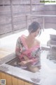 A woman in a pink kimono sitting in a hot tub.