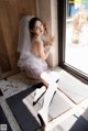 A woman in a wedding dress sitting on a window sill.