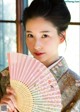 A woman in a kimono holding a pink and white fan.