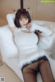 A woman in a white shirt and black stockings sitting on a white couch.