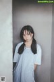 A woman in a white shirt leaning against a wall.