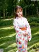 A woman in a white kimono standing in a garden.