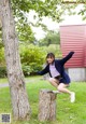 A young woman jumping on a tree stump in a park.